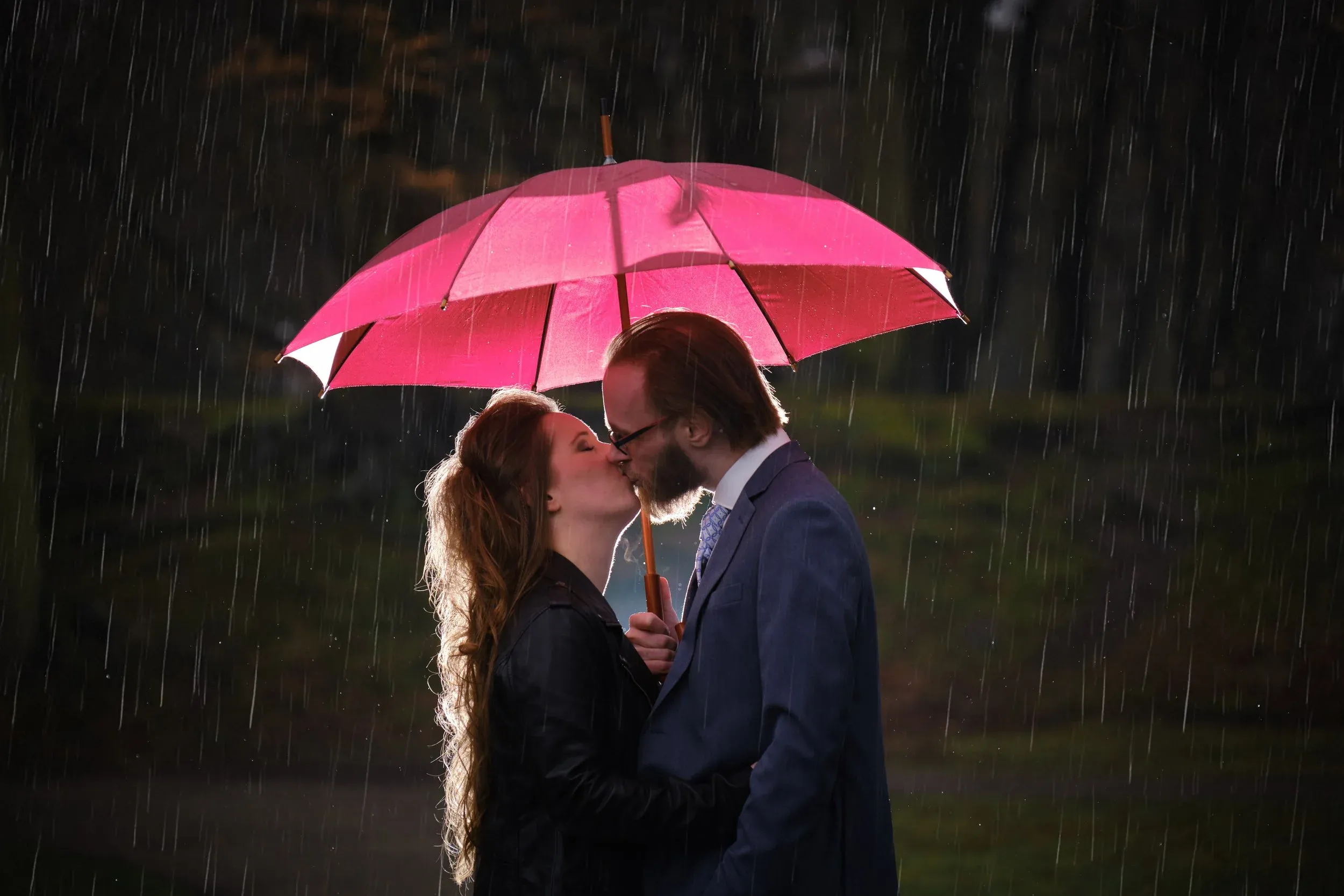 Een bruidspaar kust onder een roze paraplu in de regen