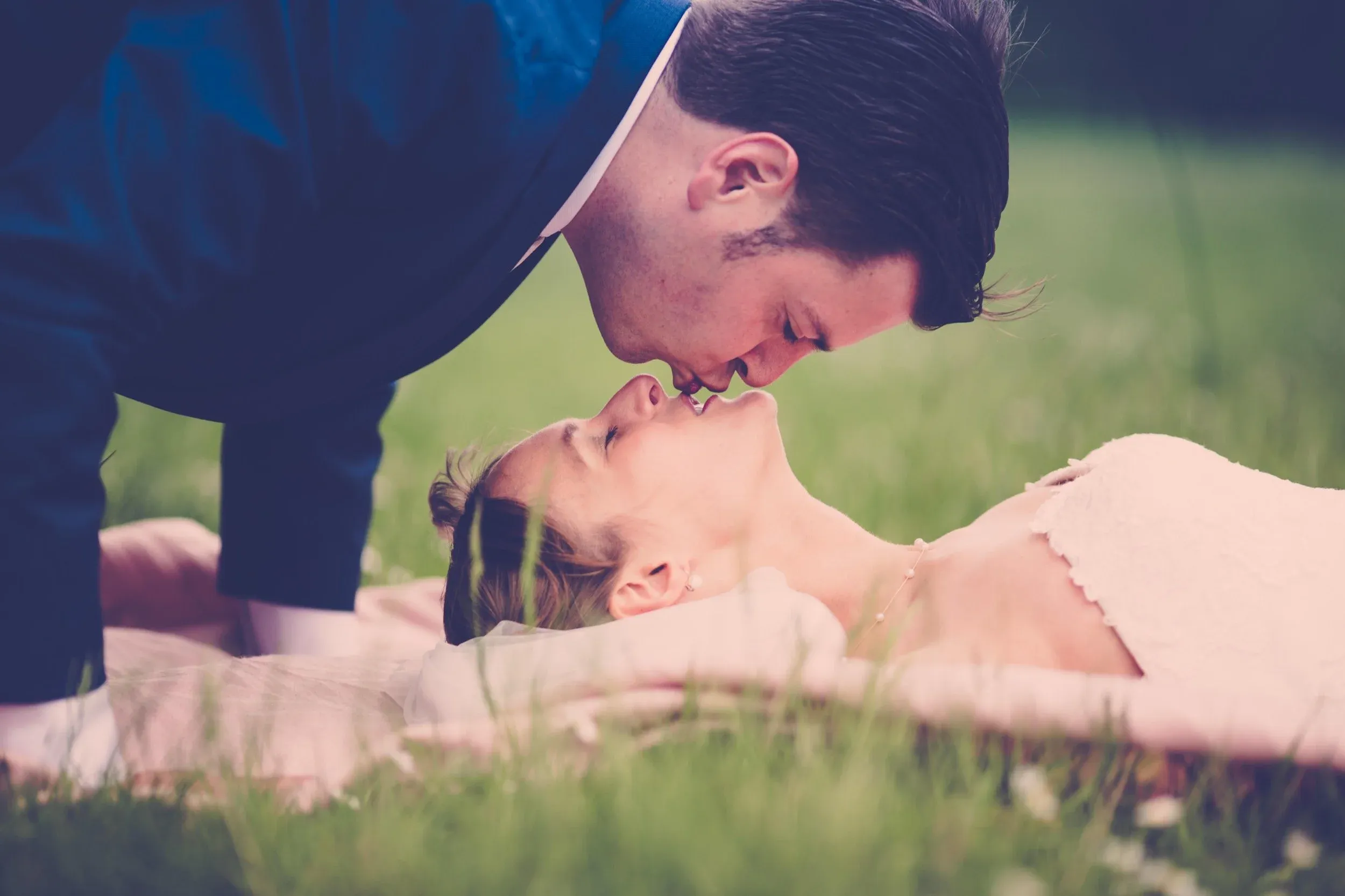Een man en een vrouw die dicht bij elkaar staan, met hun neuzen en voorhoofden tegen elkaar, mogelijk in een romantisch moment op een groene grasweide.