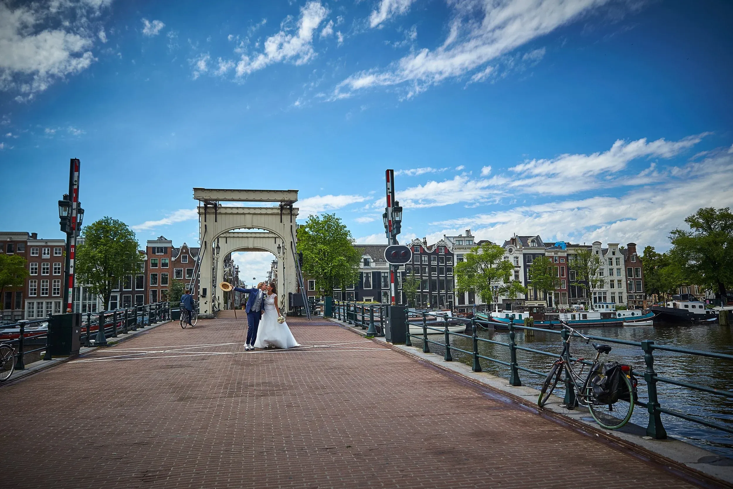 Bruidspaar midden op de Magere Brug, met grachtenpanden en een strakblauwe lucht