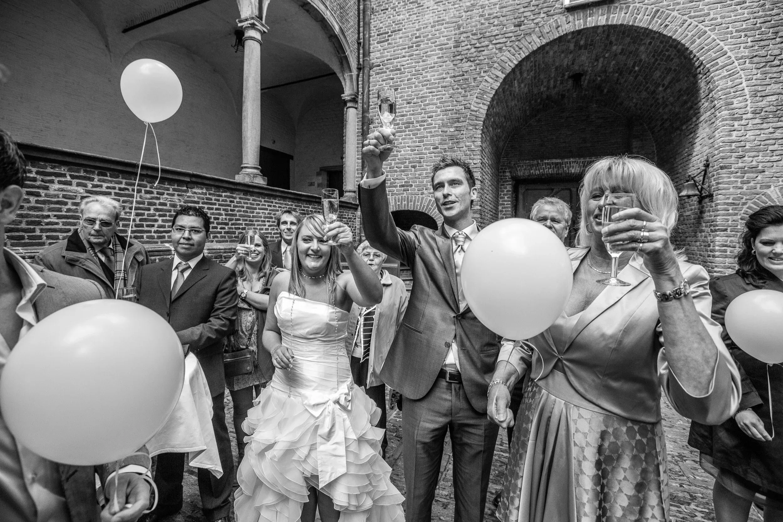 Feestend gezelschap bij een trouwfeest met ballonnen en champagne in een historische binnenplaats.