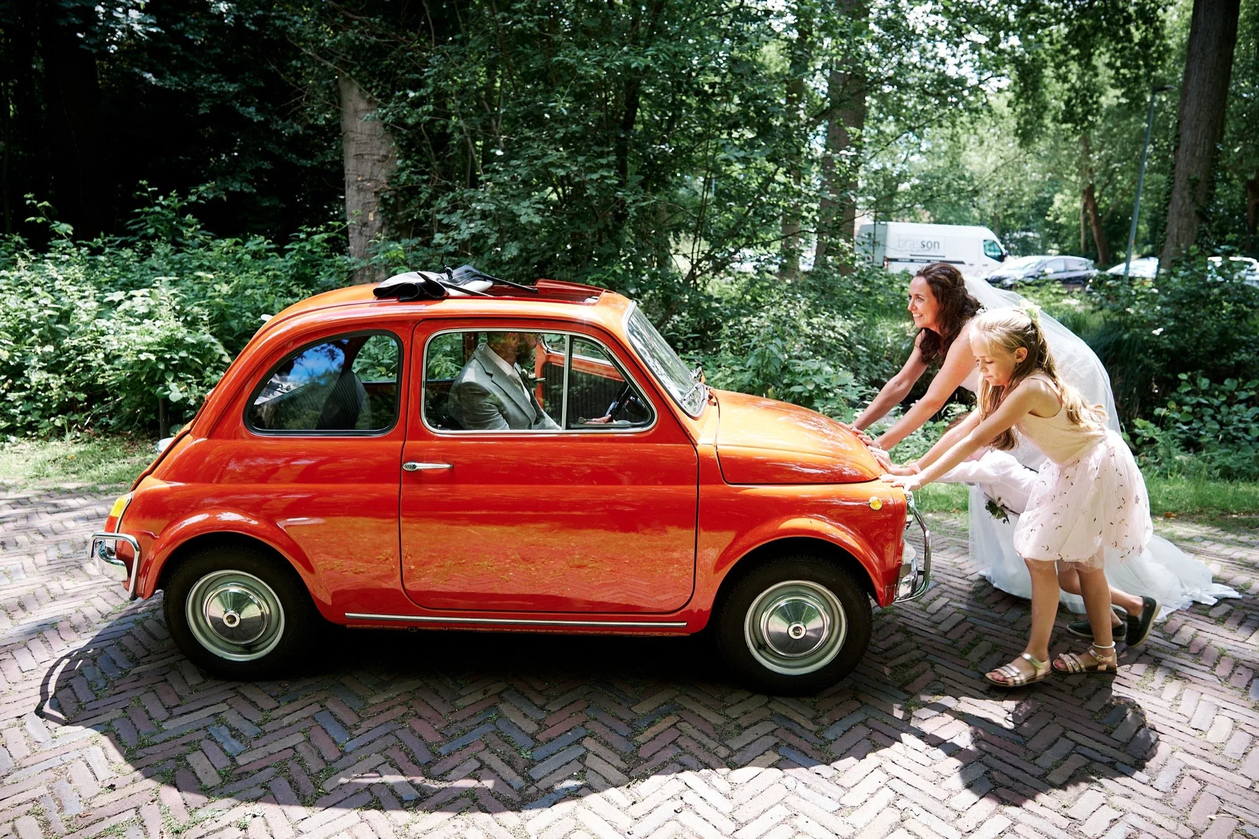 Twee vrouwen en een meisje duwen de rode Fiat 500 over het bospad