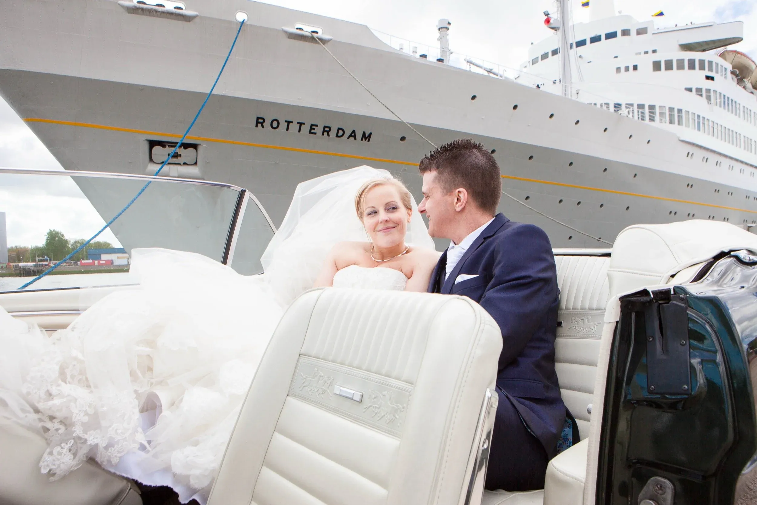 Bruidspaar in een witte cabrio met de SS Rotterdam op de achtergrond