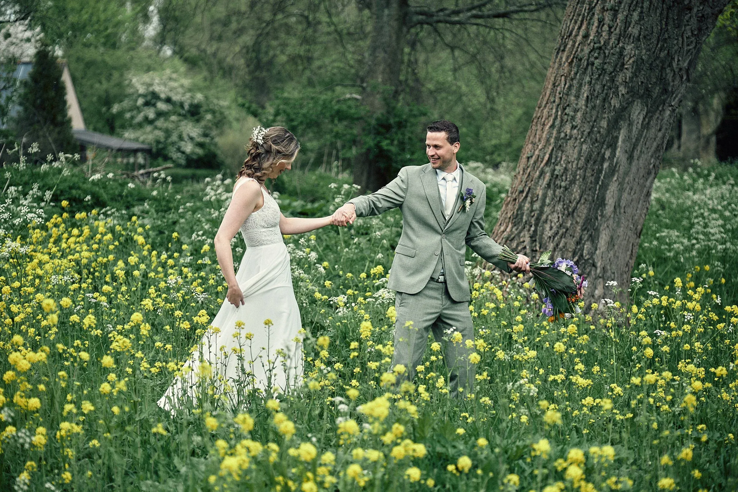 Het bruidspaar loopt hand in hand door een veld met gele bloemen