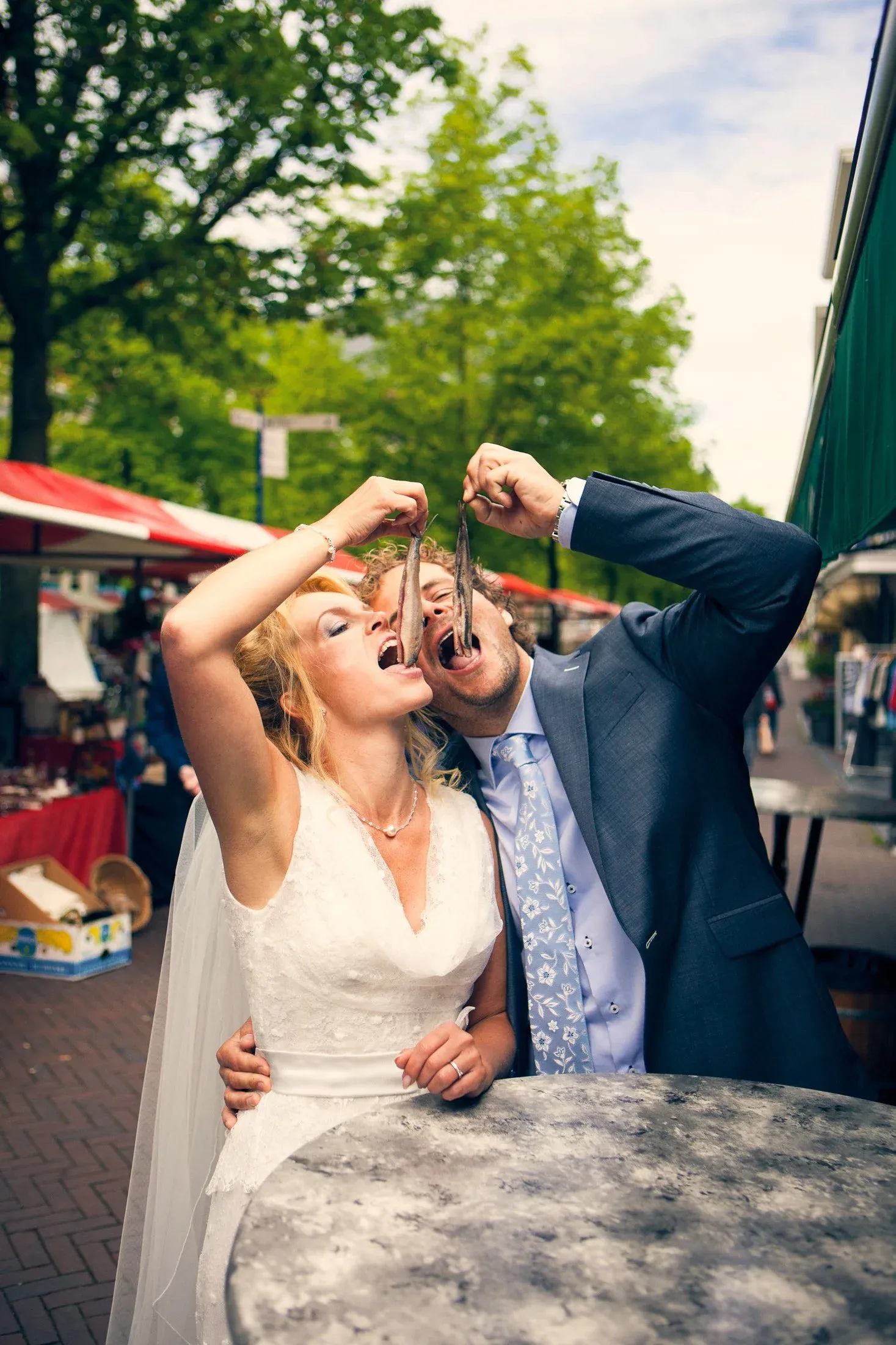 En paar in pak op een markt eten visjes samen, ze lachen en lijken plezier te hebben.
