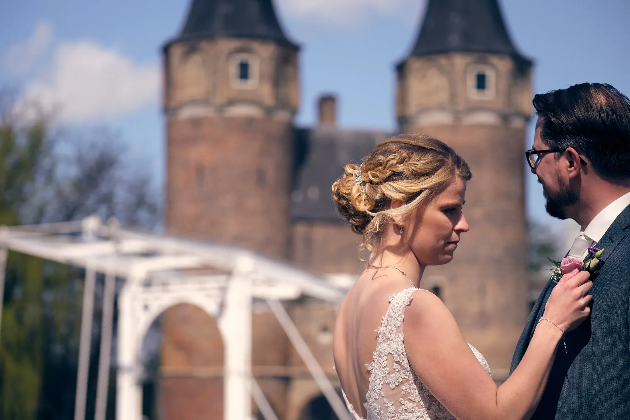 Bruidskoppel in trouwkleding staat dicht bij elkaar, met een kasteel op de achtergrond.