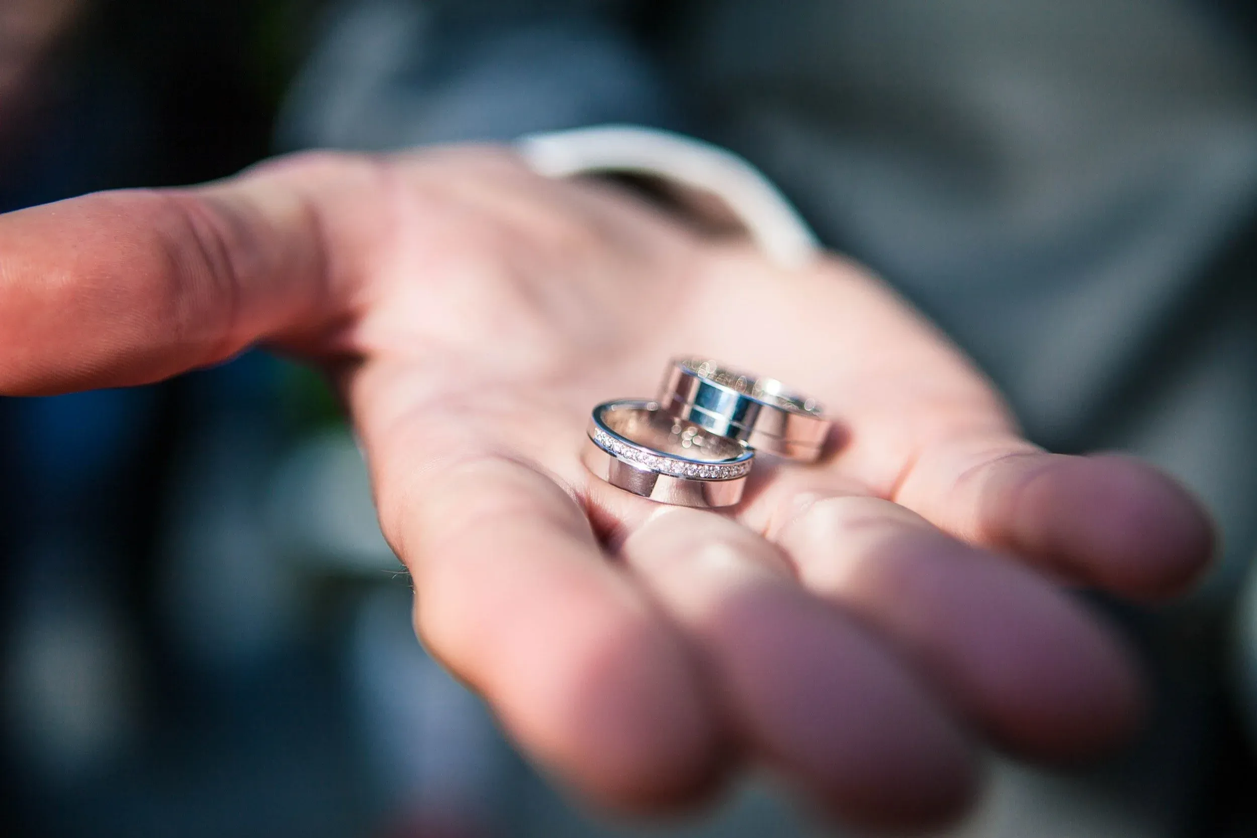 Hand met drie ringen, waaronder een verlovingsring met kleine diamanten