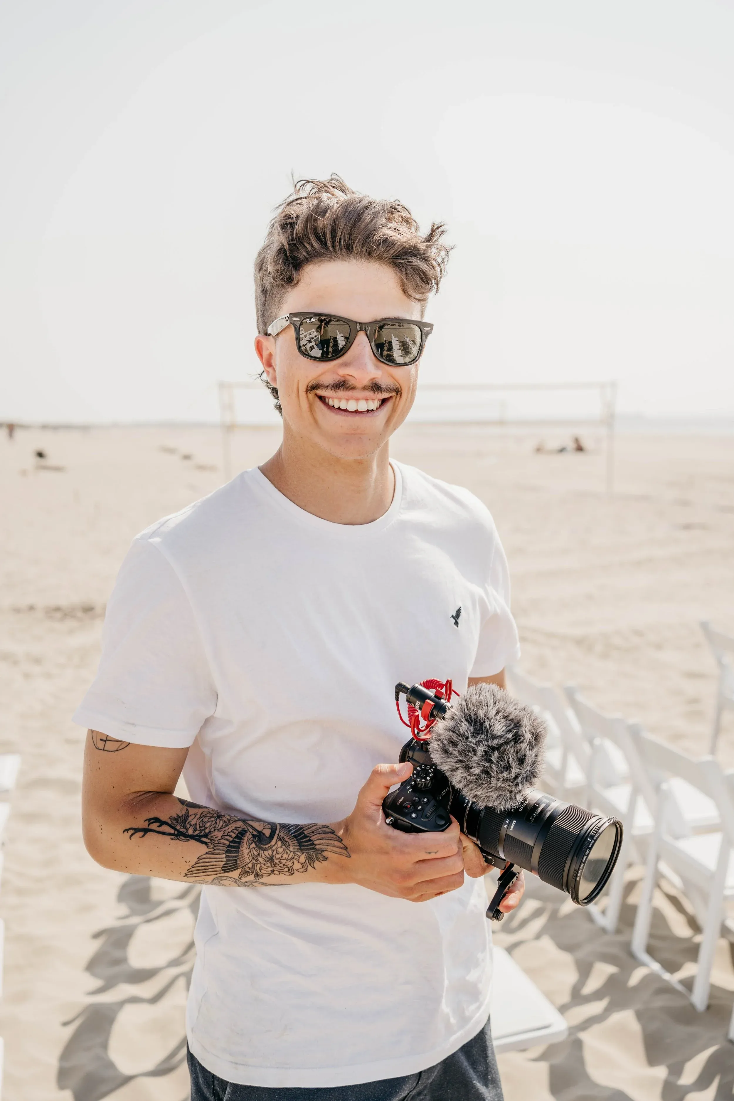 Tomas lachend op het strand, met zijn camera in de hand