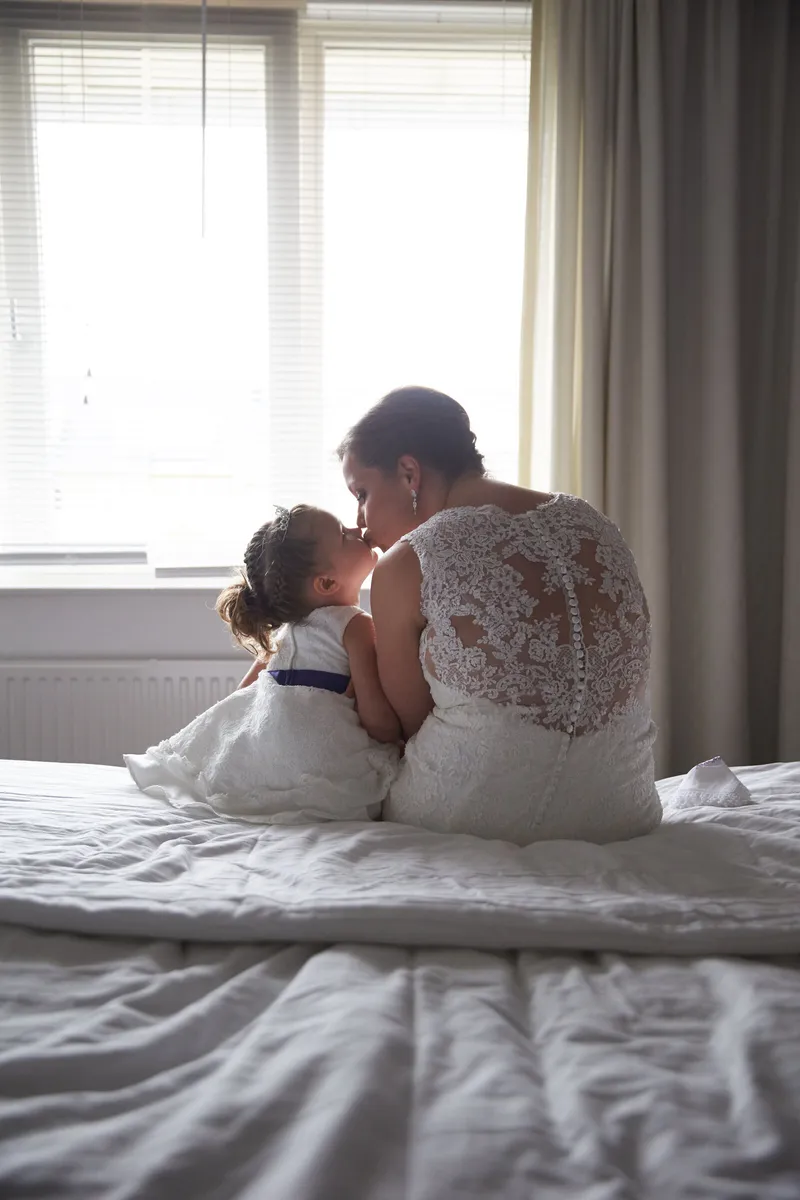 Nadine zit op het bed met een klein meisje bij het raam
