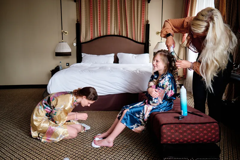 Neomi wordt gekapt in de hotelkamer, twee meisjes spelen op de vloer