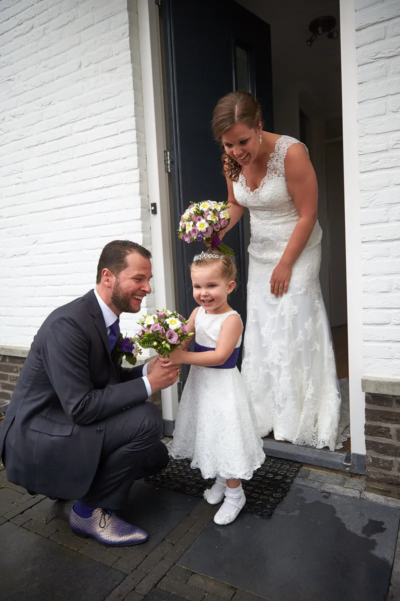 Nadine bij de voordeur, een gast knielt bij een kind met een bloemetje