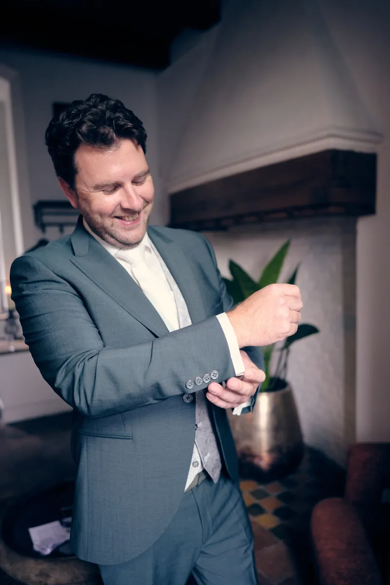 Fabian in zijn grijsblauwe pak doet lachend zijn manchet dicht