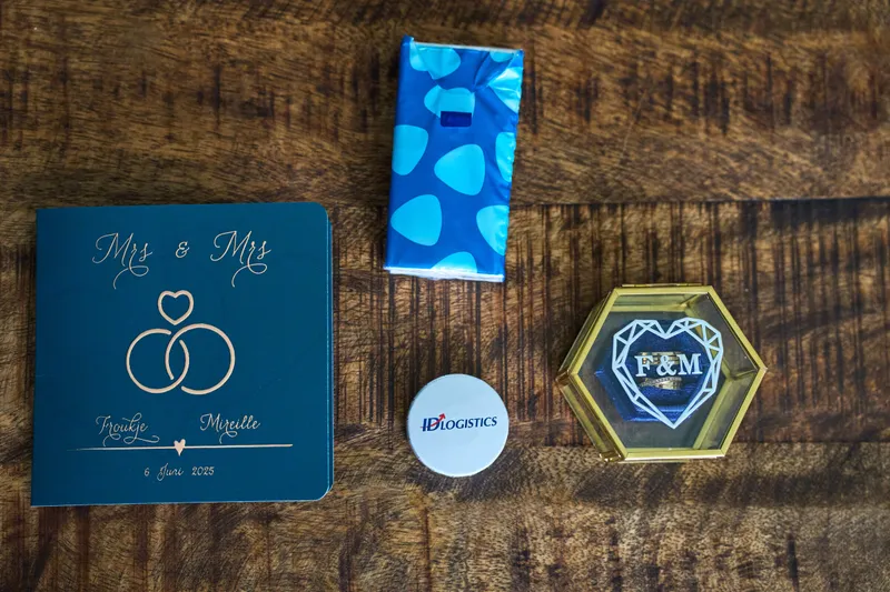 Een kaart met Mrs & Mrs, de ringen en een badge met F&M op een houten tafel
