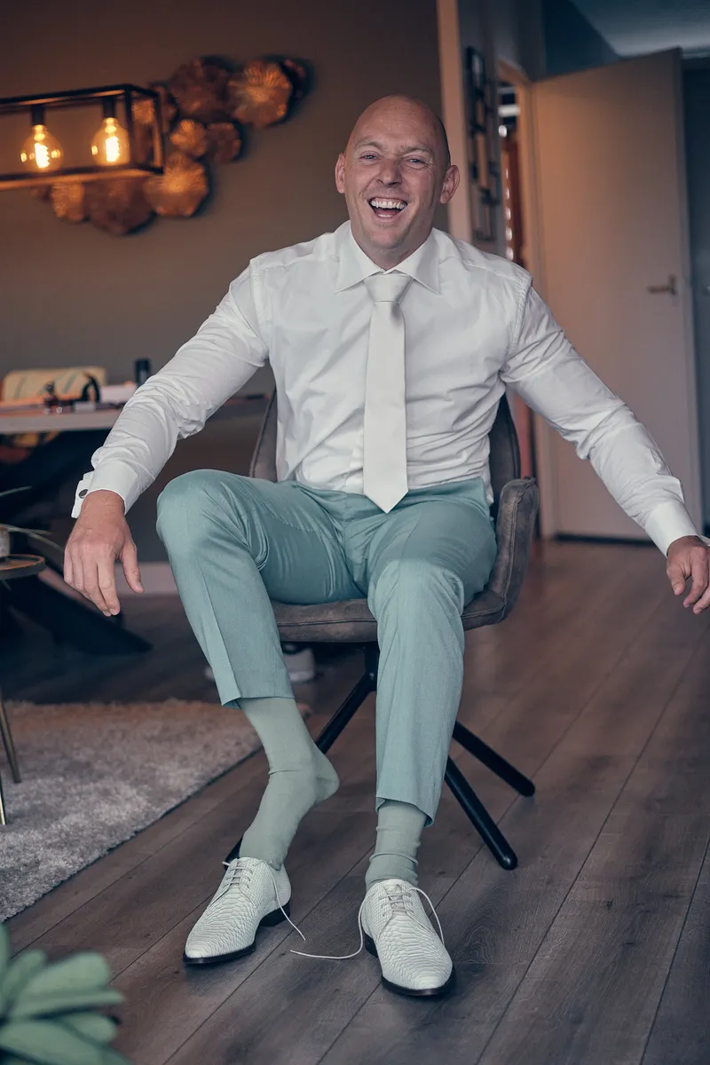 Dennis zit lachend op een stoel in zijn mintgroene broek