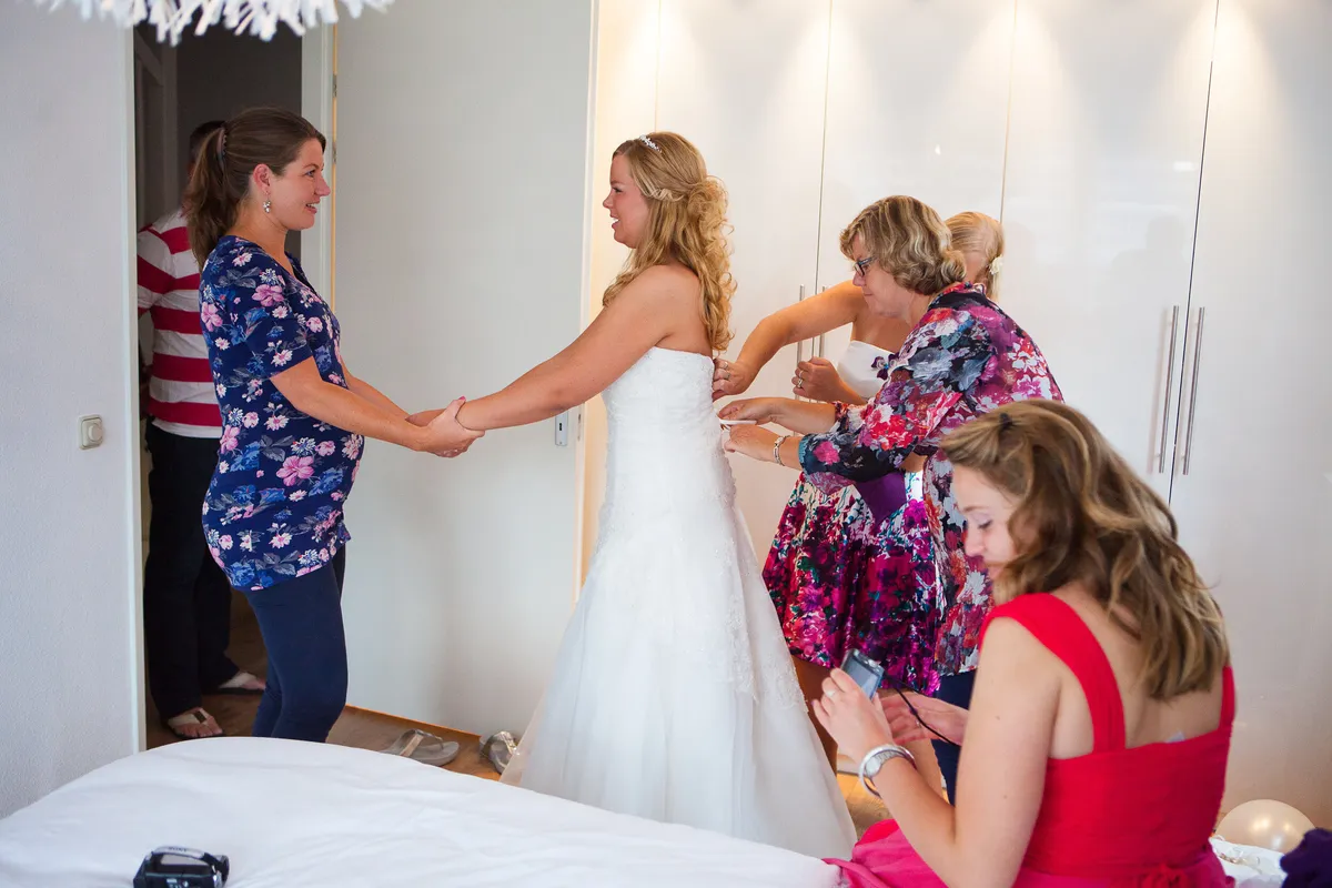 Vriendinnen en familie helpen Esther met het dichtmaken van de trouwjurk