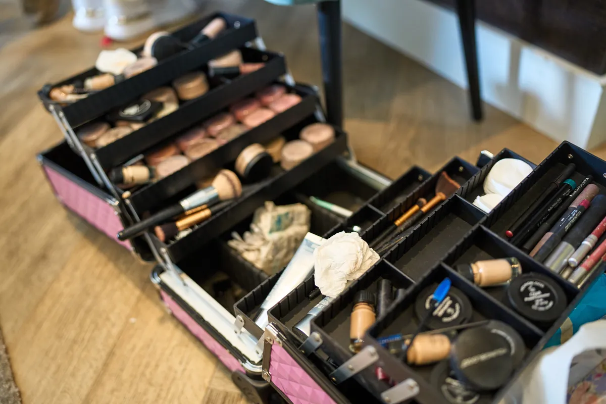 Een open make-upkoffer vol kwasten en poeders op een houten tafel