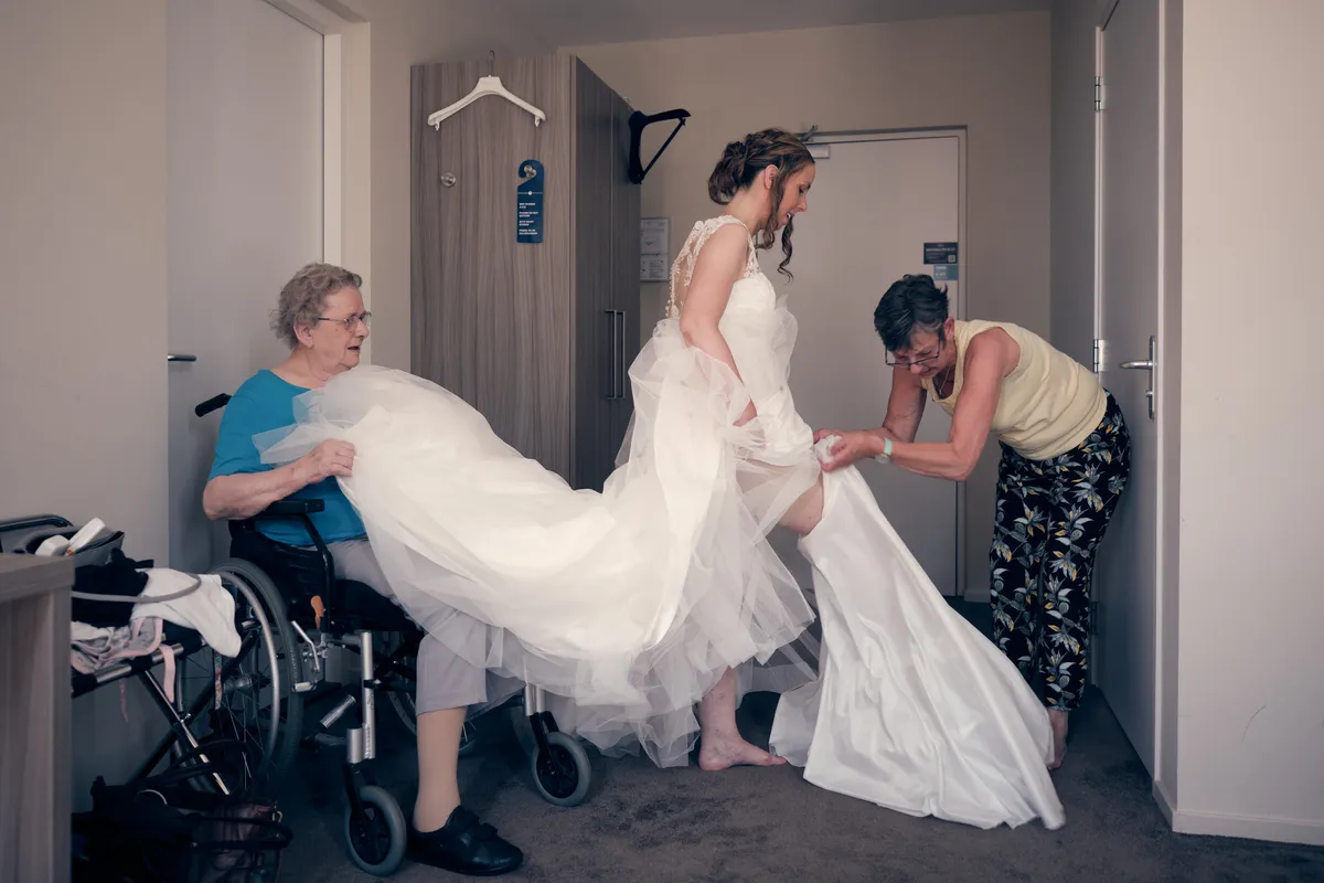 Ilja in haar trouwjurk op de hotelkamer, haar oma en moeder helpen met de jurk