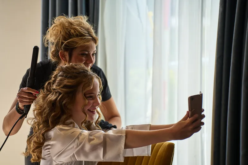 De kapper steekt het haar op terwijl de bruid een selfie maakt