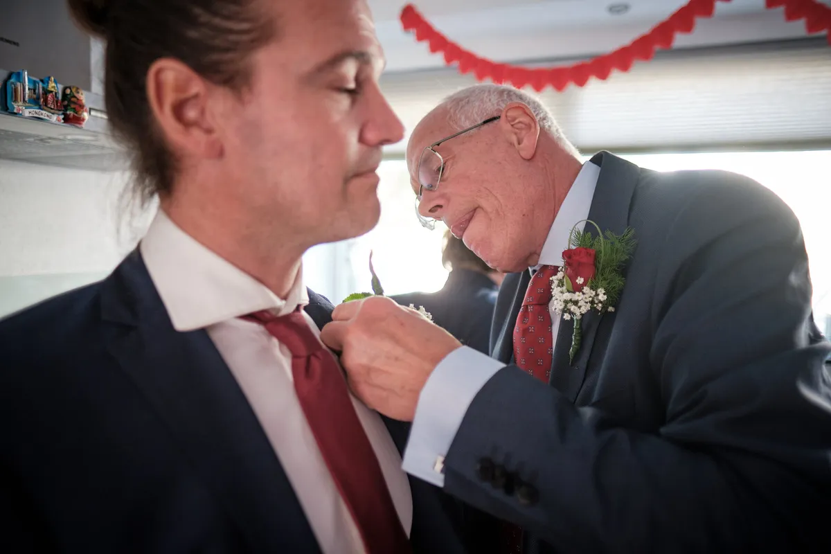 Een oudere man speldt een roos op het jasje