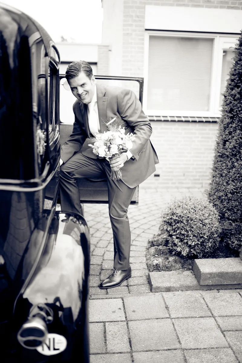 Stefan zit met het boeket op de treeplank van de oldtimer, zwart-wit
