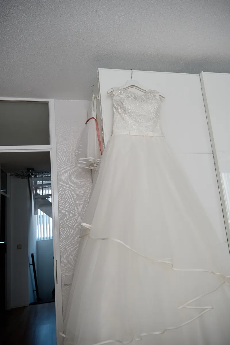 De trouwjurk hangt klaar aan de kastdeur