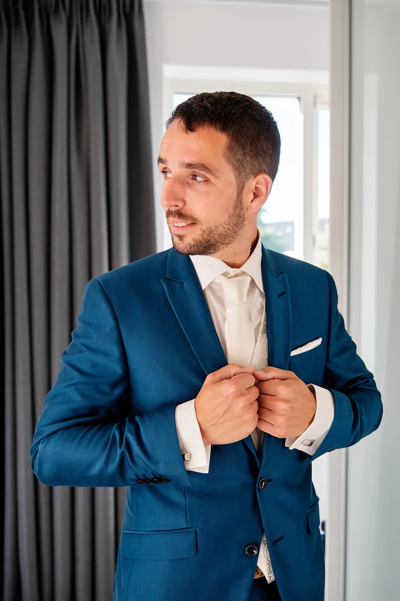 Jeroen knoopt zijn blauwe colbert dicht bij het raam
