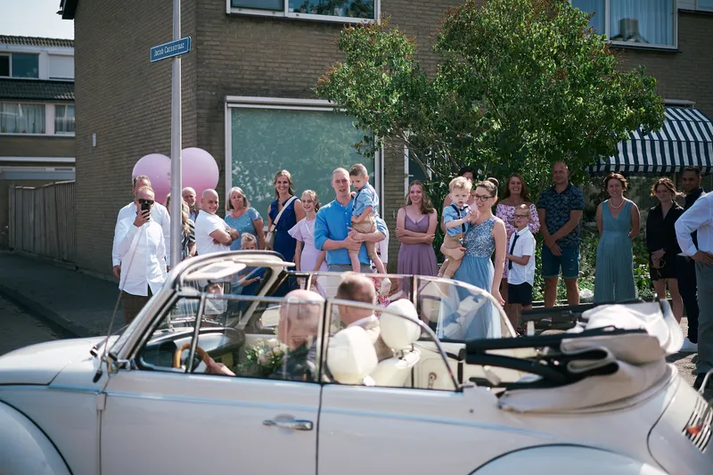 De witte Kever cabrio komt de straat in, de gasten staan te wachten