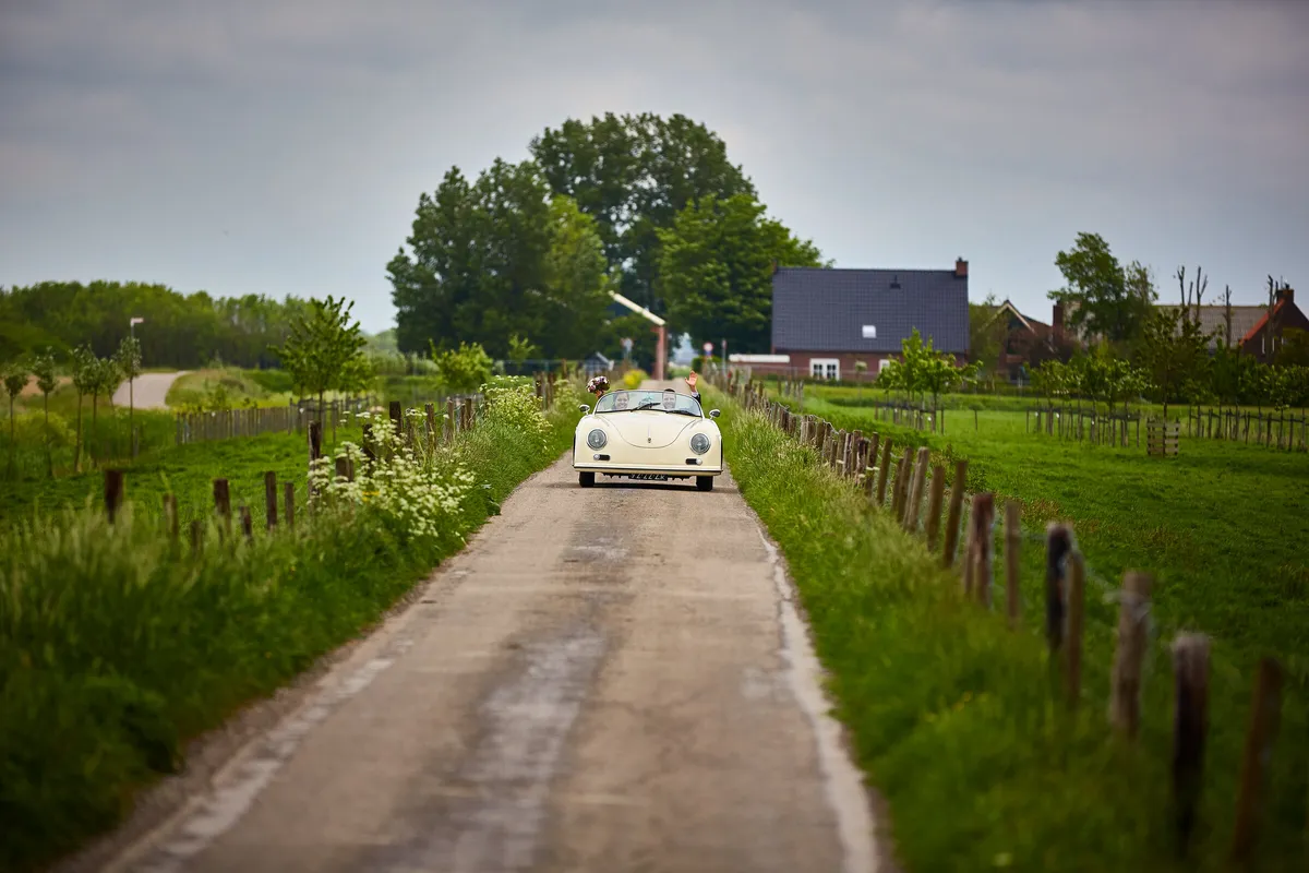 De witte Porsche op een smalle weg tussen de weilanden
