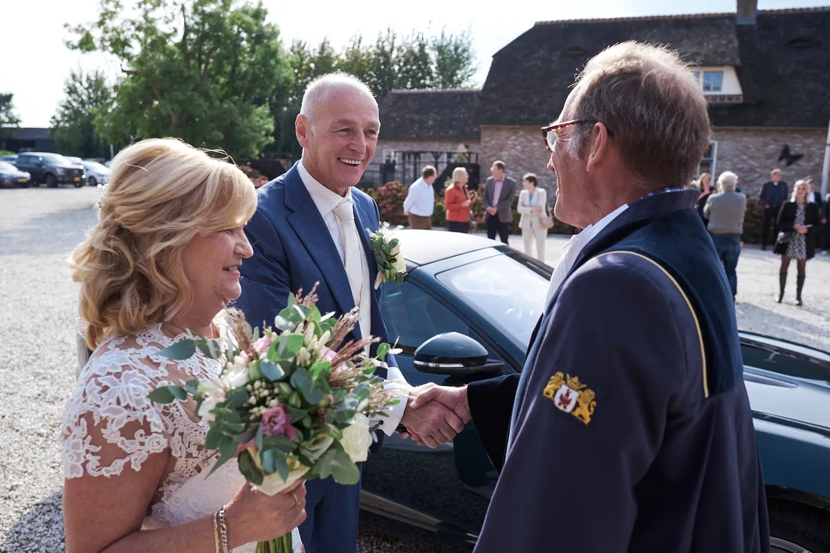 De trouwambtenaar geeft Jopie en Cees een hand bij aankomst