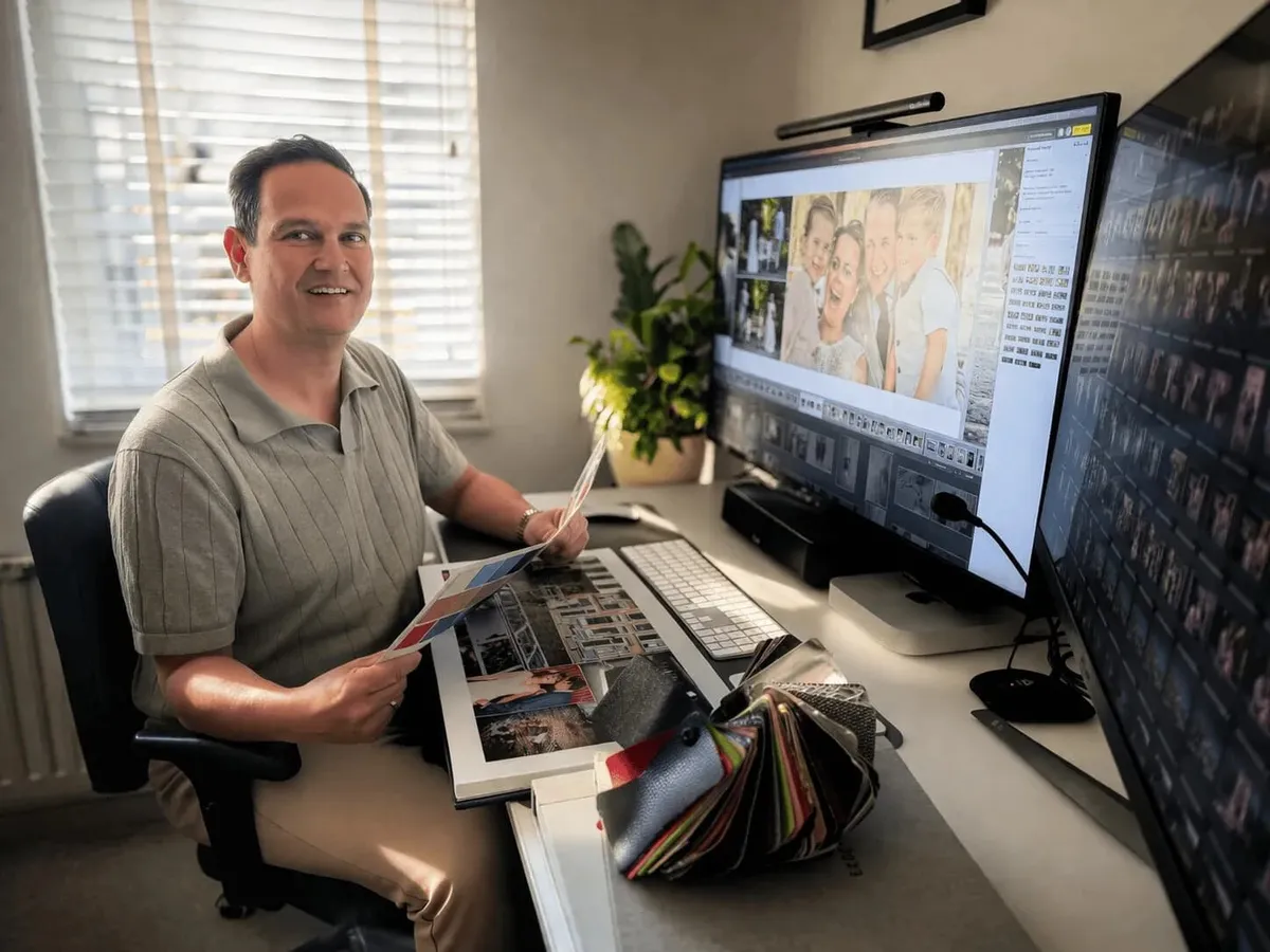 Stefan ontwerpt een trouwalbum aan zijn bureau, met het ontwerp op het scherm en proefdrukken in zijn hand