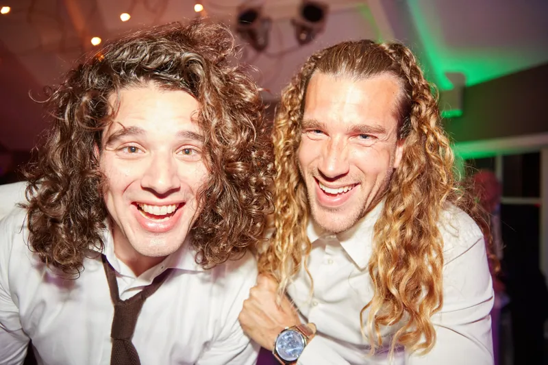 Twee gasten met krullen lachen in de camera