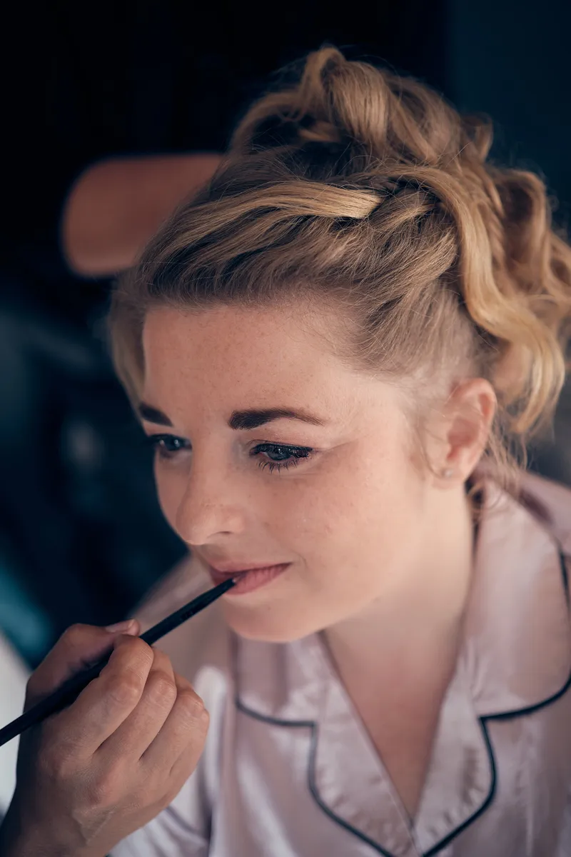 Angelique kijkt omlaag terwijl haar lippen worden opgemaakt