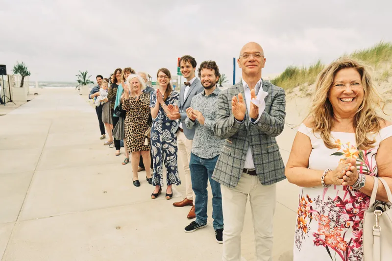 Gasten staan in een rij op het strand en klappen voor het bruidspaar