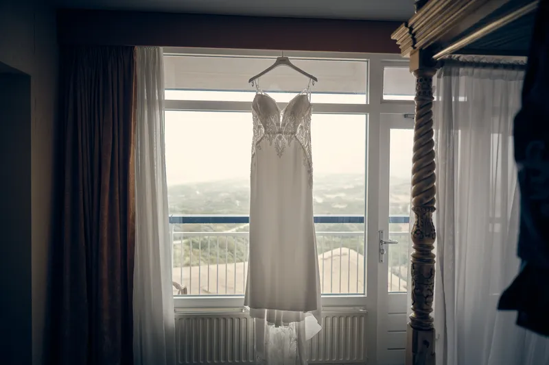De trouwjurk hangt bij het raam van de hotelkamer, met uitzicht op de duinen
