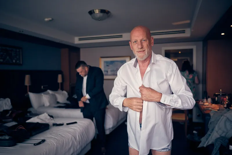 Patrick knoopt zijn overhemd dicht in de hotelkamer