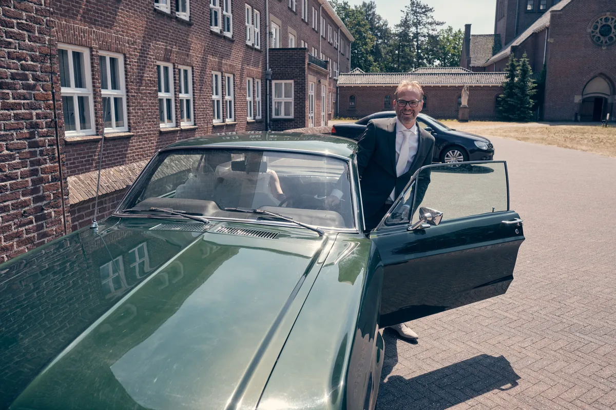 Mike houdt de deur van de groene Ford Mustang open voor het hotel