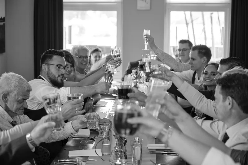 De gasten heffen hun glas aan de lange tafel, zwart-wit