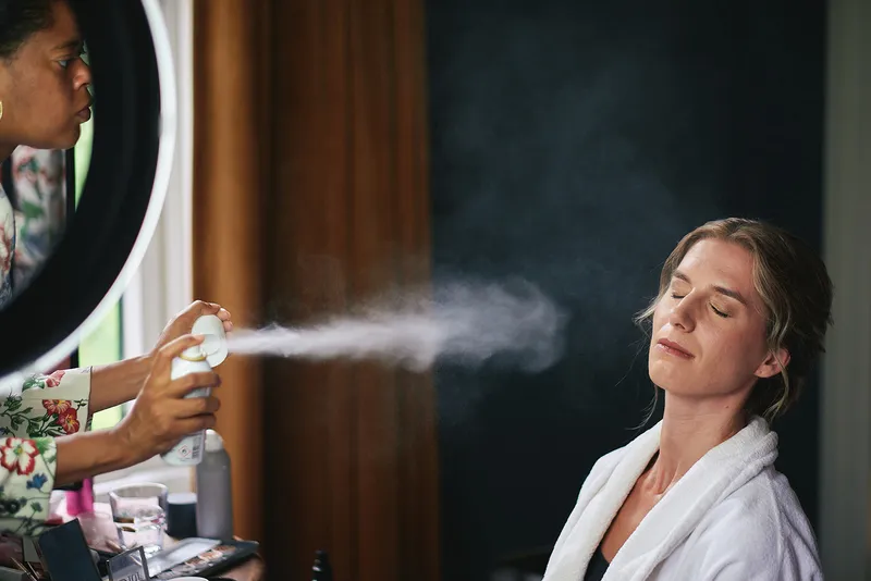 Kariens kapsel wordt afgewerkt met een wolk haarspray tegen de donkere muur