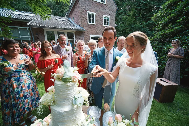 Karien en Niels snijden samen de taart aan, met het huis op de achtergrond