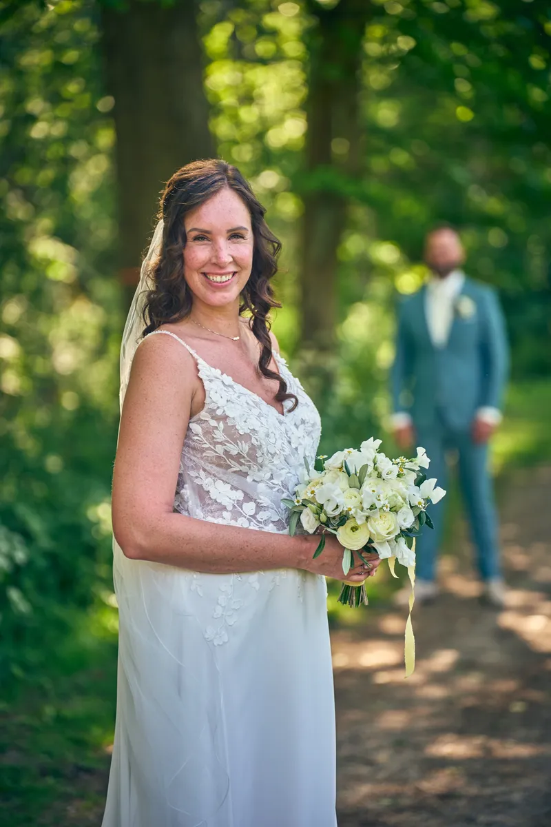 Michelle lacht met haar boeket op het bospad, Barrie loopt achter haar