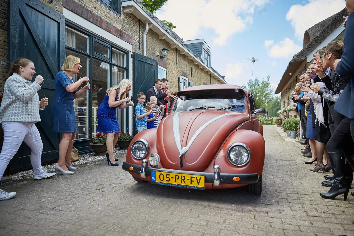 De rode Kever rijdt langs de zwaaiende gasten