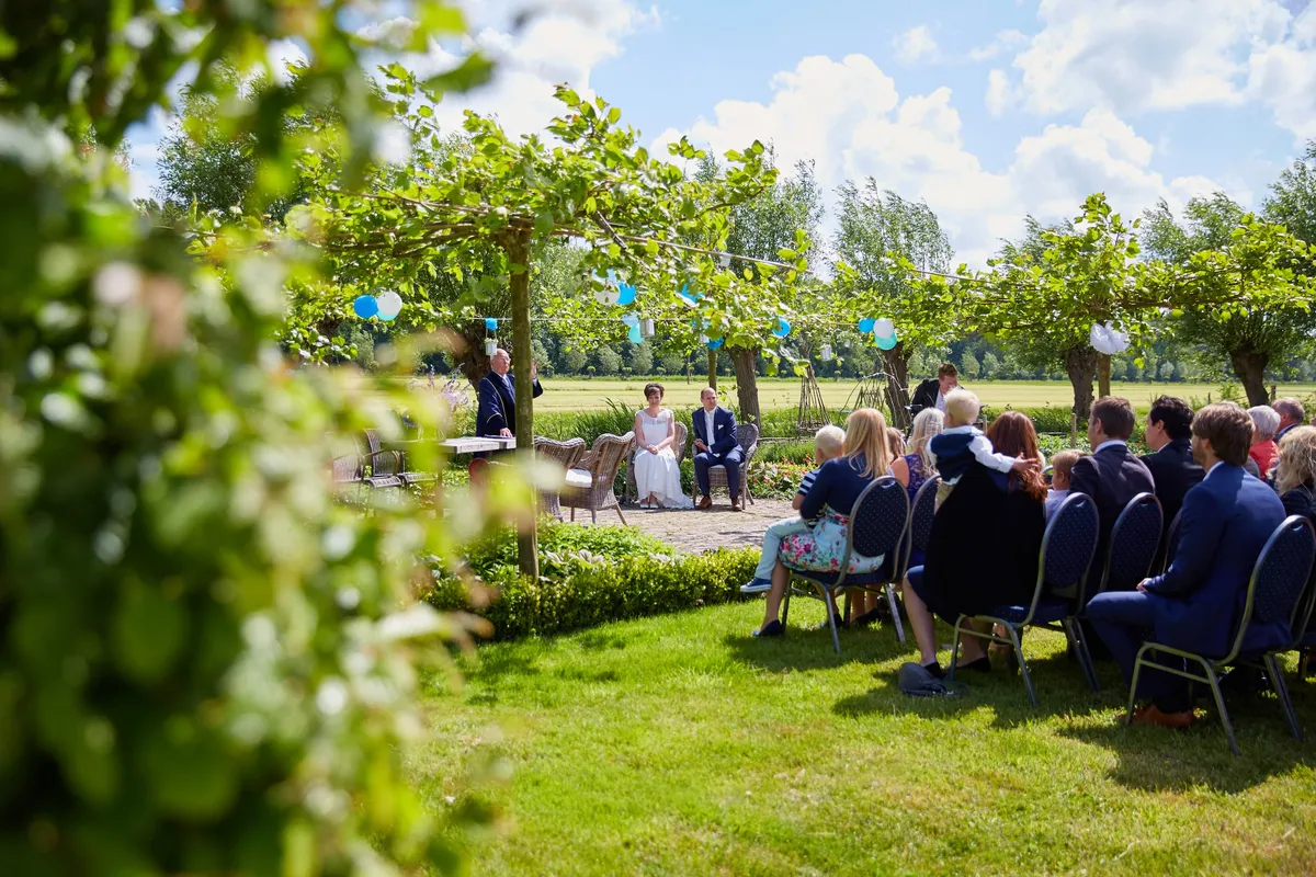 De tuin met het bruidspaar vooraan en de gasten op stoelen