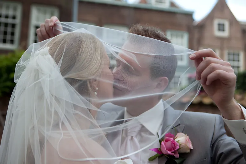 Loes en Jan kussen achter de sluier, met oude huizen op de achtergrond