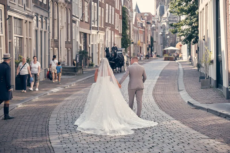 Jordy en Jacky lopen door een straat met kinderkopjes, de koets erachter