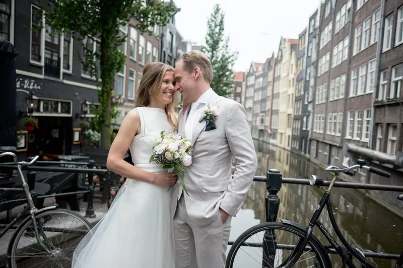 Mary en Jasper lachen aan een gracht, met fietsen en grachtenpanden