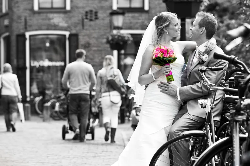 Loes en Jan leunen tegen fietsen in een drukke straat, in zwart-wit met een gekleurd boeket