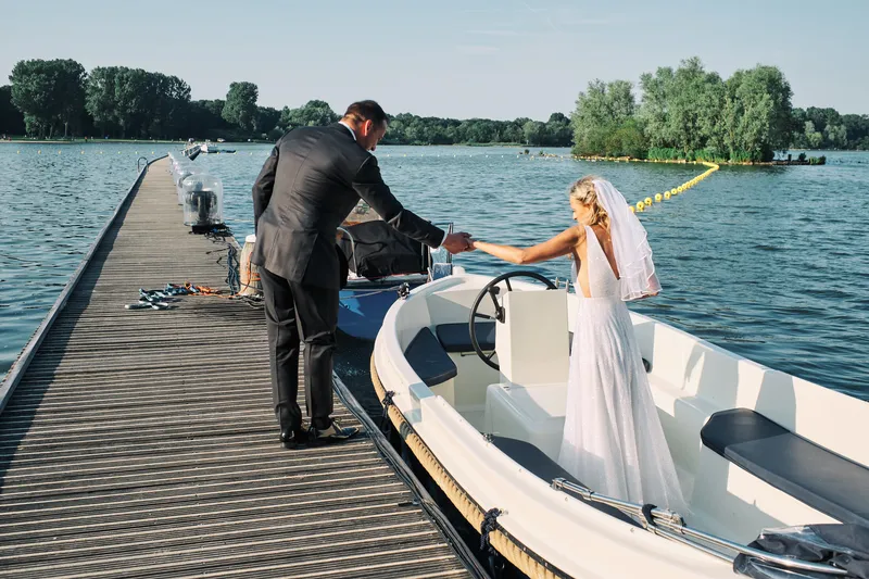 Op een steiger aan de Kralingse Plas helpt de bruidegom de bruid in een sloep