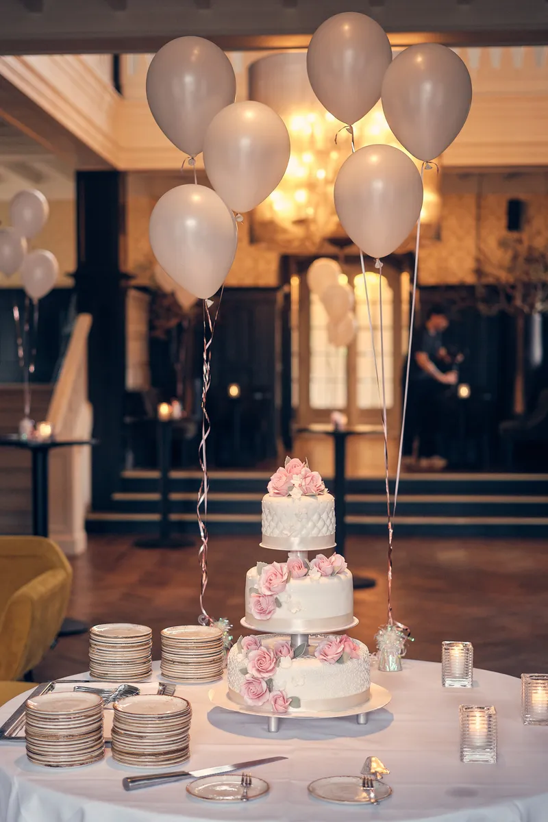 De bruidstaart met roze rozen in de hal, met witte ballonnen