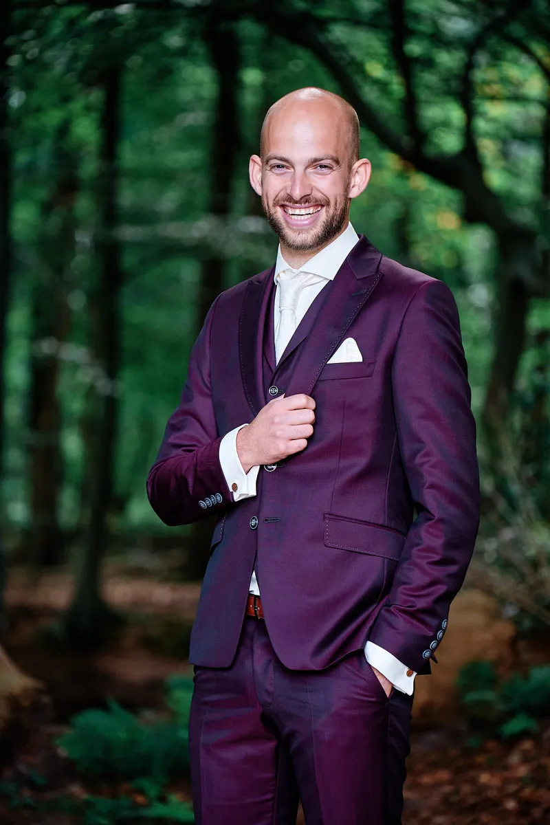 Simon lacht in zijn paarse pak in het bos
