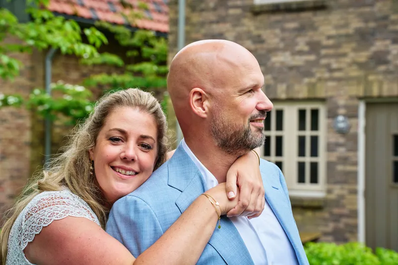 Annemarie slaat haar armen om Jan heen voor een bakstenen gevel