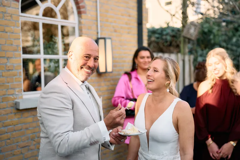 Brian voert Danitsja een stukje taart, de gasten lachen